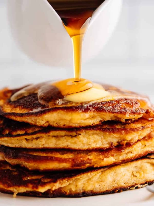 pouring maple syrup over a stack of Almond Flour Banana Pancakes