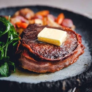 acon Wrapped Filet Mignon served on a dark gray plate with vegetables photographed at an angle.