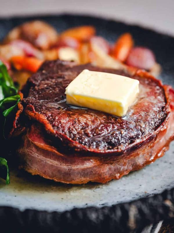 acon Wrapped Filet Mignon served on a dark gray plate with vegetables photographed at an angle.