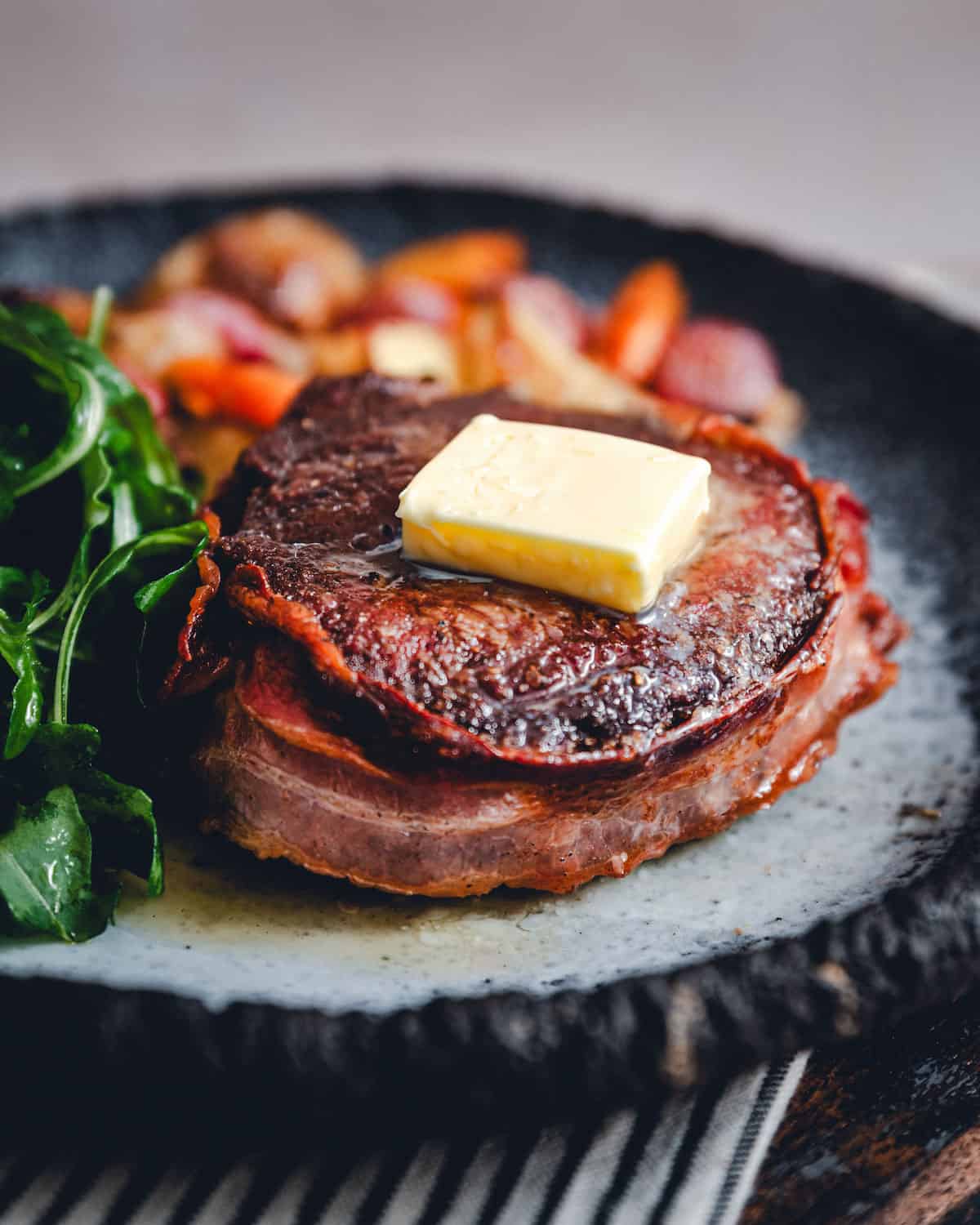 Bacon Wrapped Filet Mignon served on a dark gray plate with vegetables.