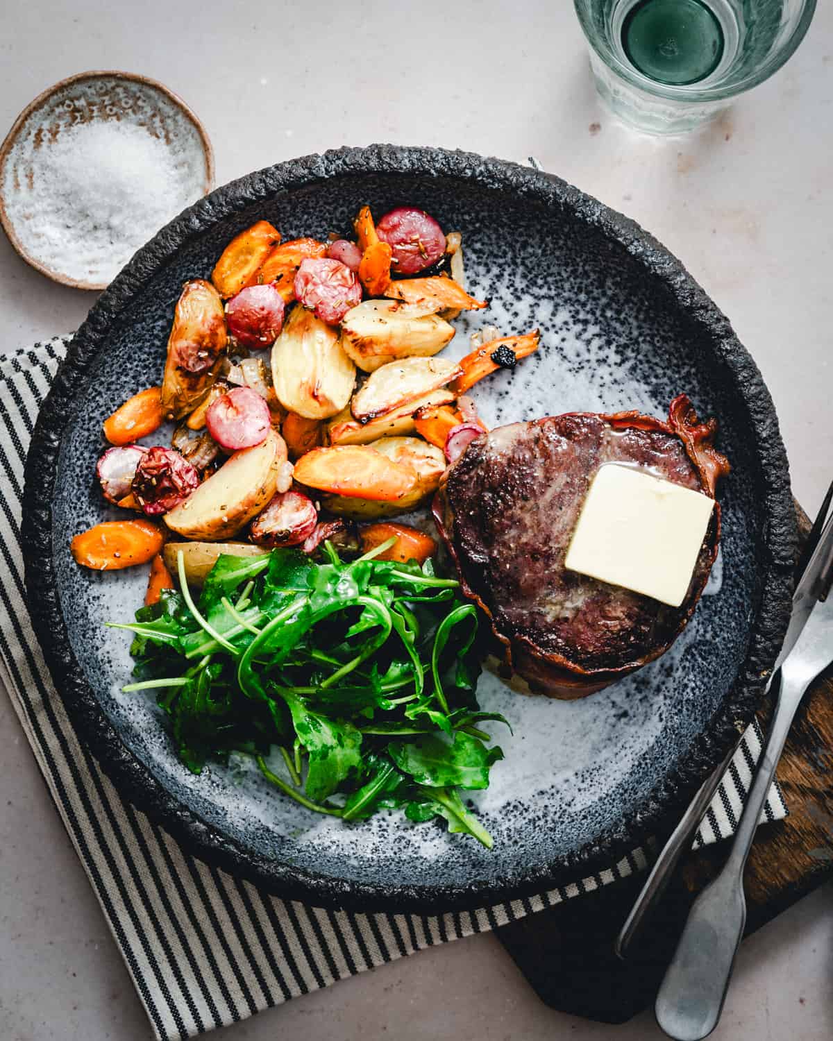 Bacon Wrapped Filet Mignon served on a dark gray plate with vegetables and photographed from the top.