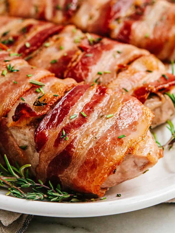 Bacon Wrapped Pork Chops served on a white oval platter with rosemary sprigs.