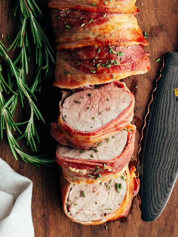 Bacon Wrapped Pork Tenderloin sliced and served on a wooden board and photographed from overhead.