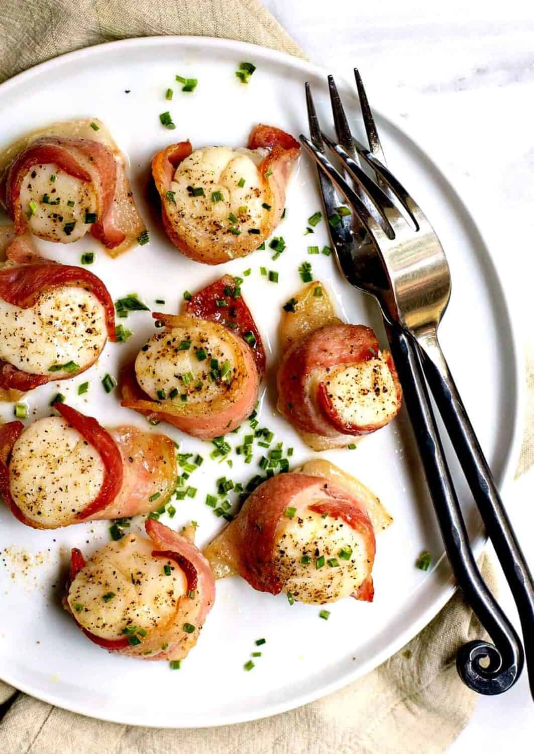 Bacon Wrapped Scallops served on a round white plate with two forks