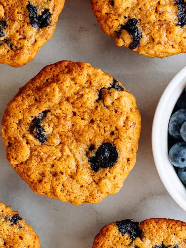 Banana Blueberry Oatmeal Muffins on a white marble board with a bowl of fresh blueberries.