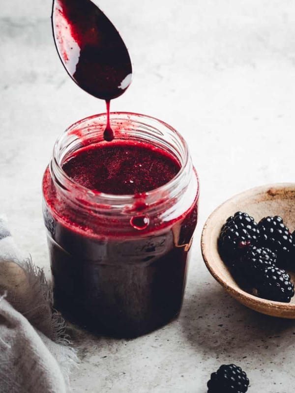 Blackberry Syrup dripping off a spoon into a glass jar.