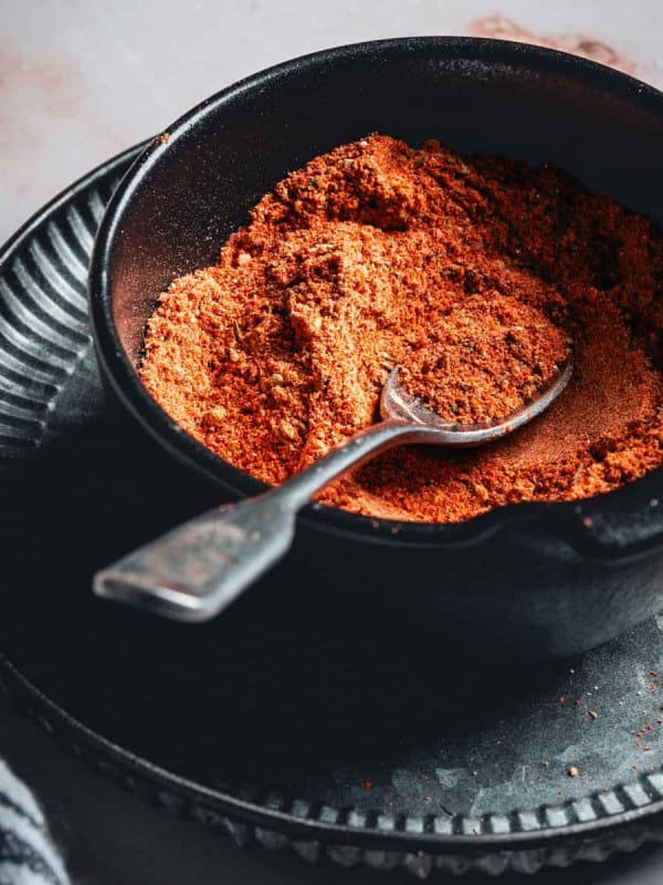 Homemade Blackened Seasoning in a black bowl with a silver spoon photographed at an angle.