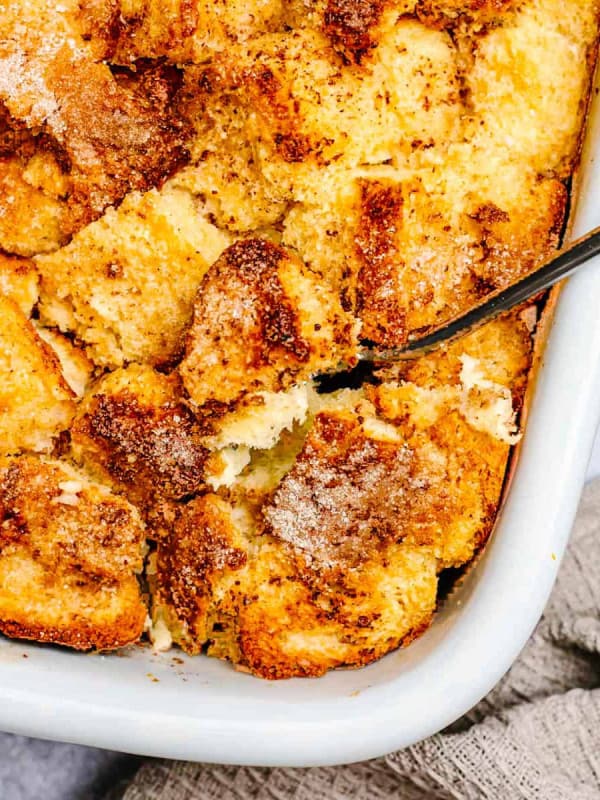 Brioche French Toast Casserole in a white ceramic baking dish with a serving spoon photographed from overhead.