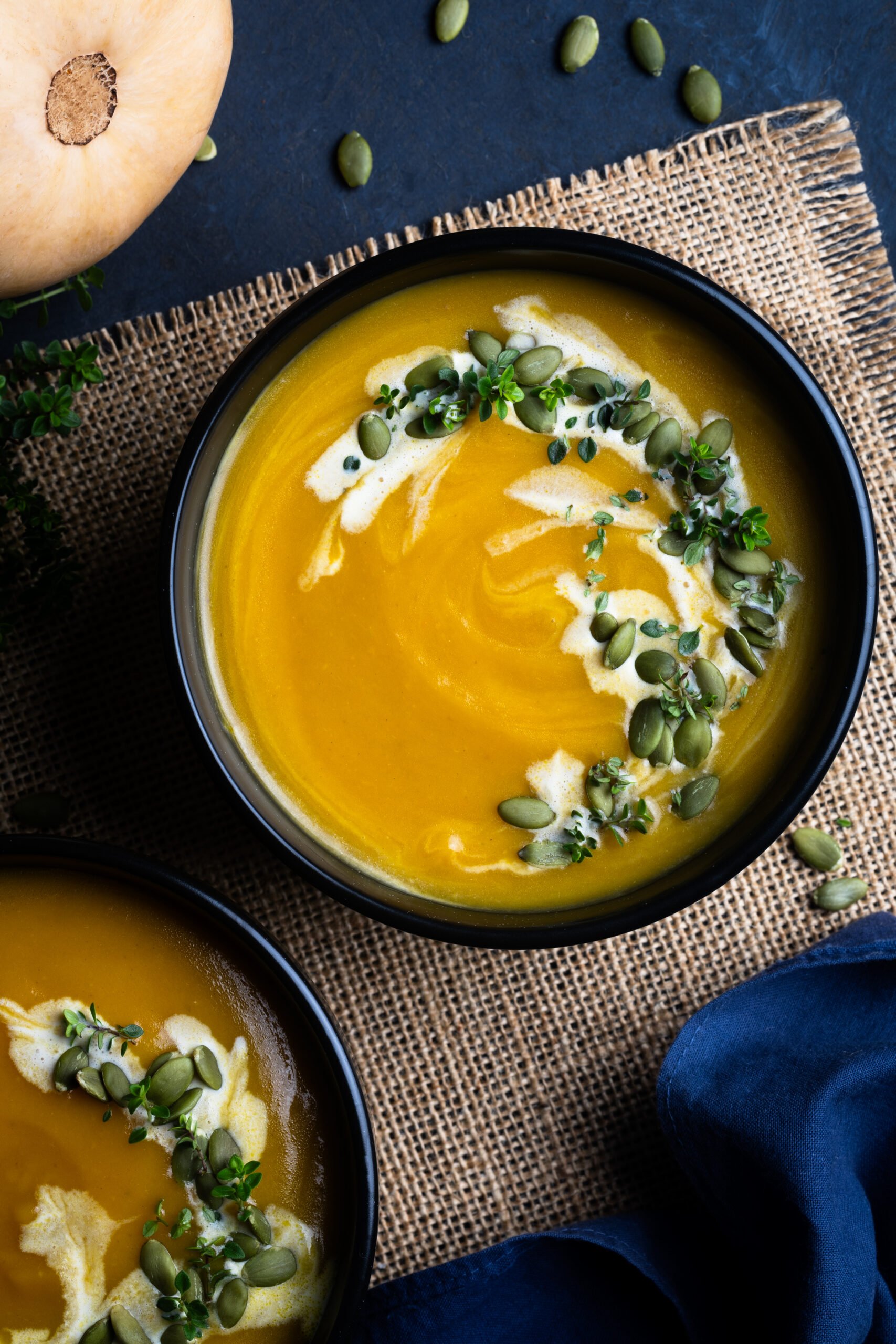 Two bowls of Butternut Squash Bisque served in black bowls and photographed from the top.