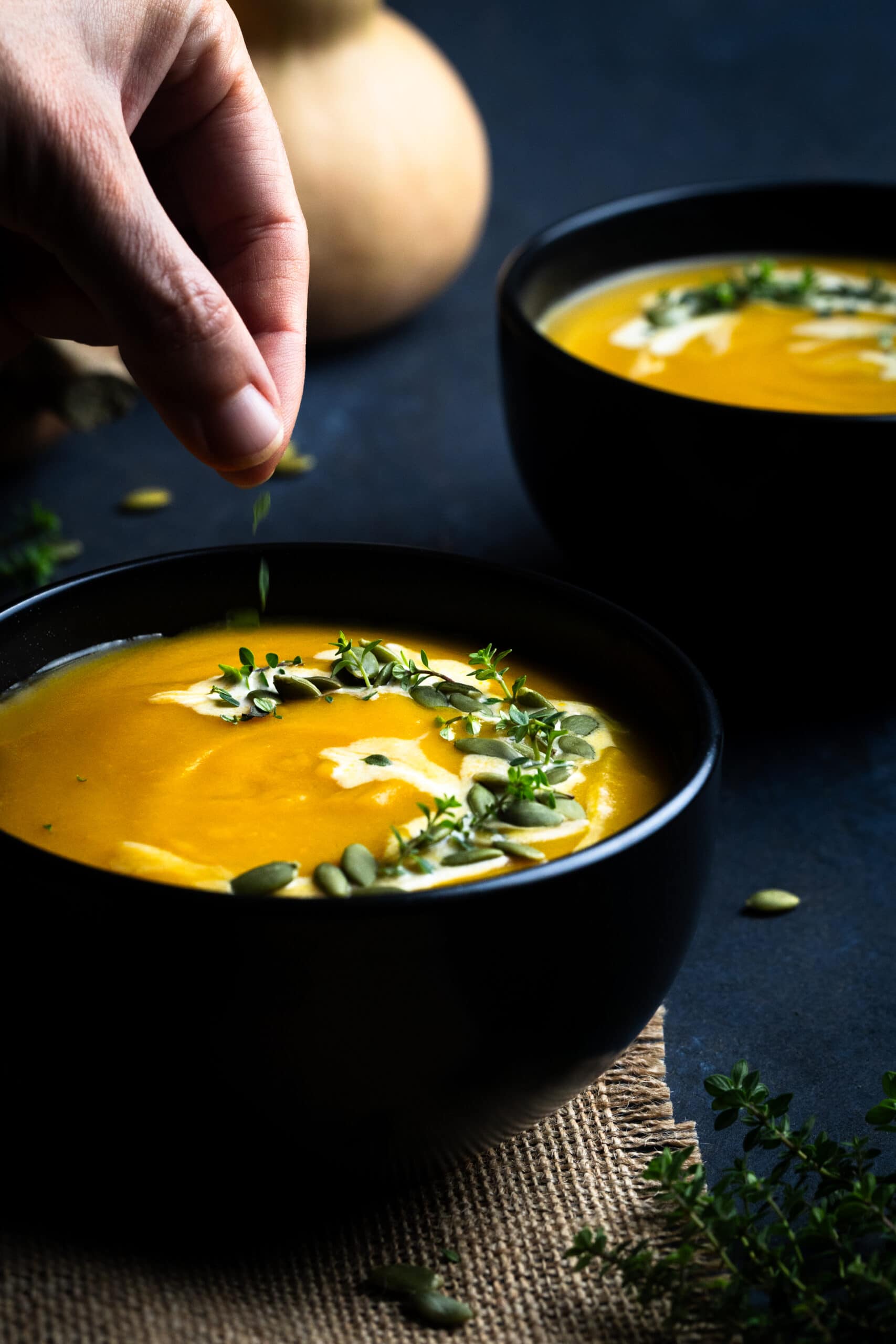 Sprinkling pumkin seeds over Butternut Squash Bisque served in a black bowl and photographed at an angle.