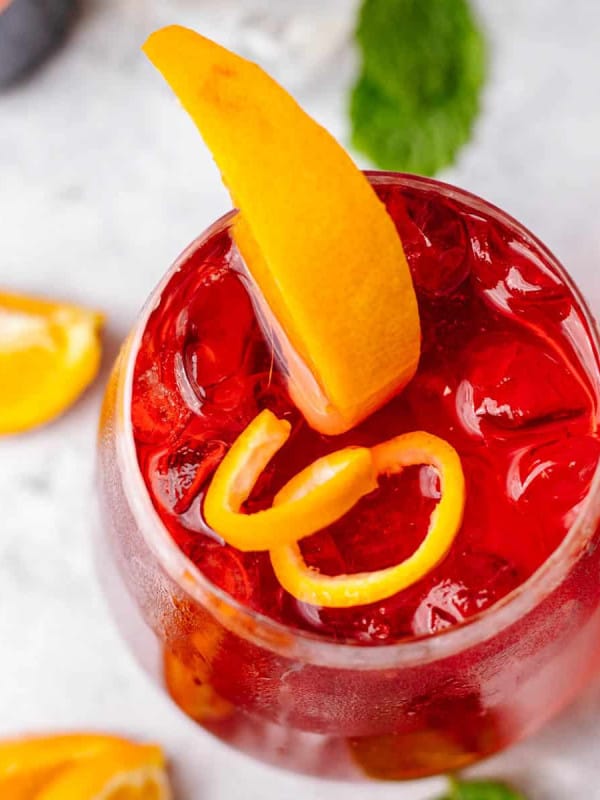 Campari Spritz cocktail photographed from the top on a white surface with orange slices and ice cubes.