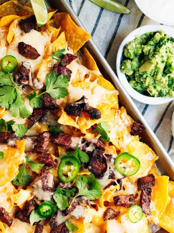 Carne Asada Nachos served in a rimmed baking sheet with guacamole salsa and sour cream.