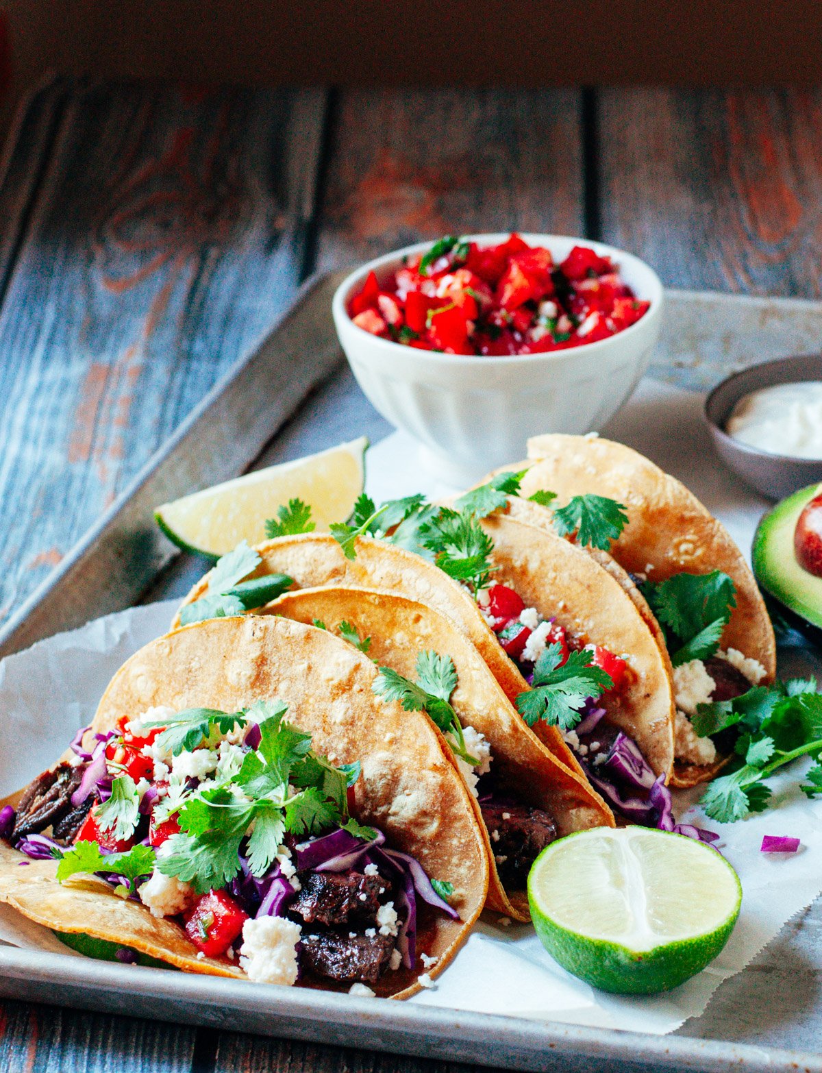 Carne Asada Tacos served on a tray with pico de gallo, lime wedges and sour cream.