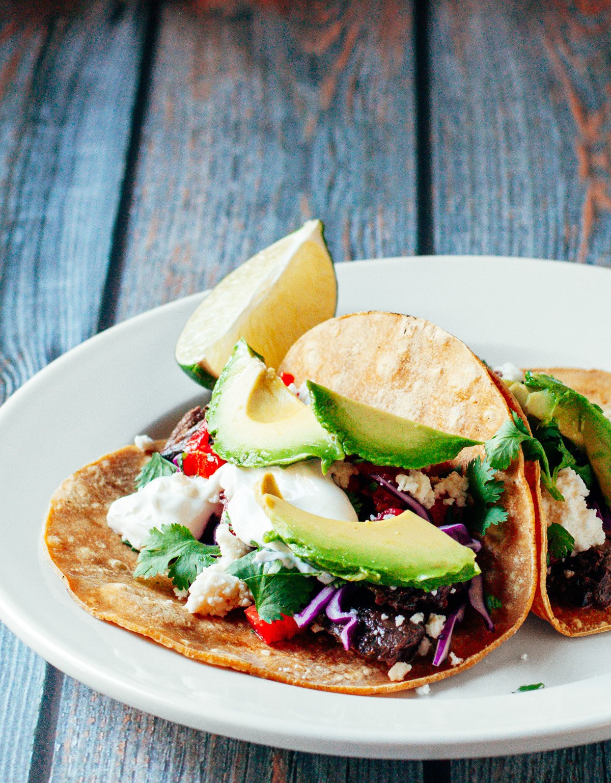 Carne Asada Tacos served on a white plate with a lime wedge.