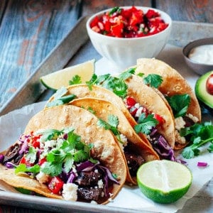 Carne Asada Tacos served on a tray with pico de gallo, lime wedges and sour cream.