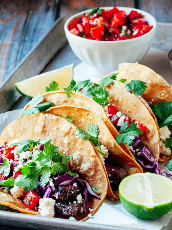 Carne Asada Tacos served on a tray with pico de gallo, lime wedges and sour cream.