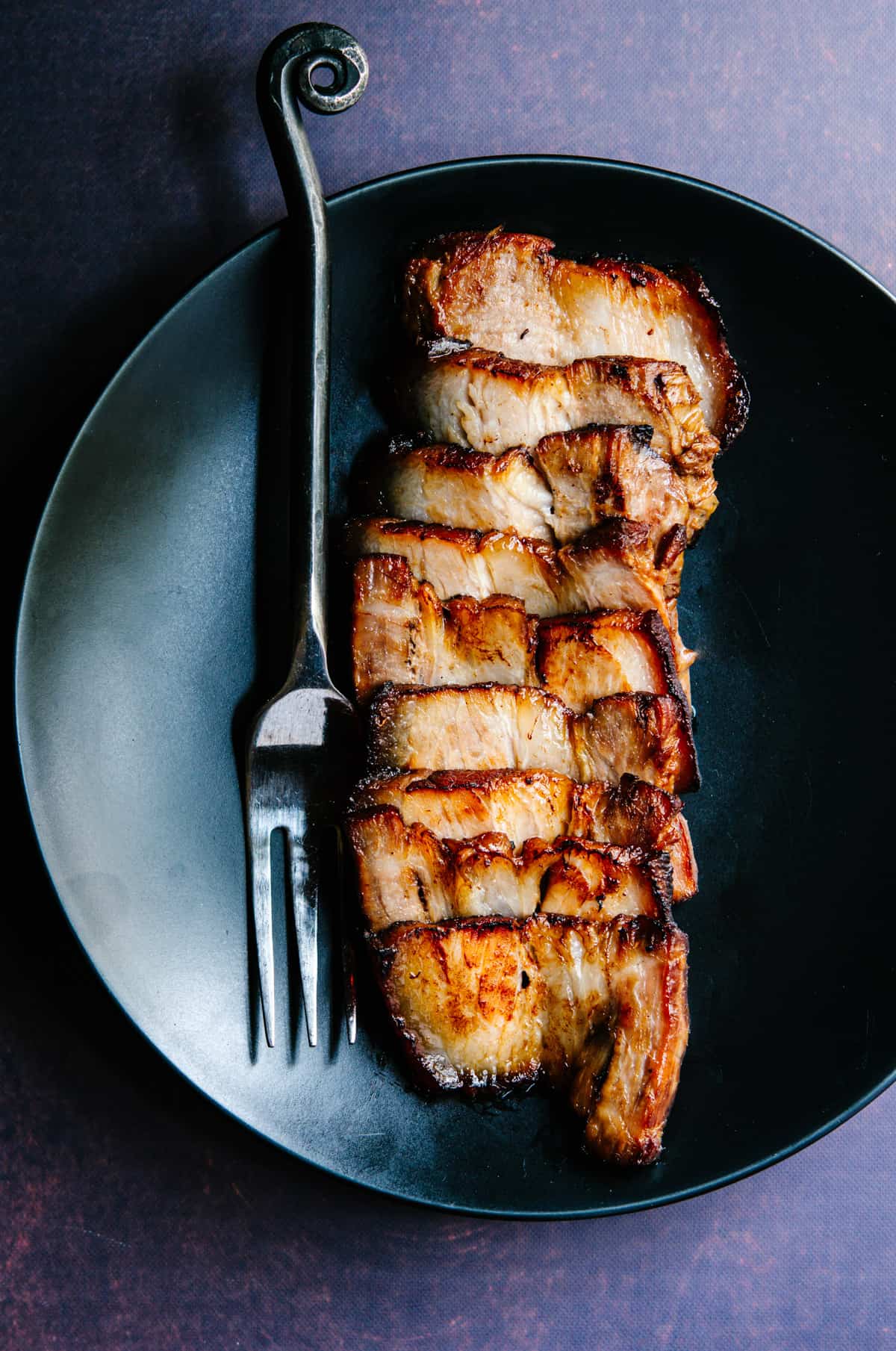 Chashu Pork served on a black plate with a serving fork photographed from above