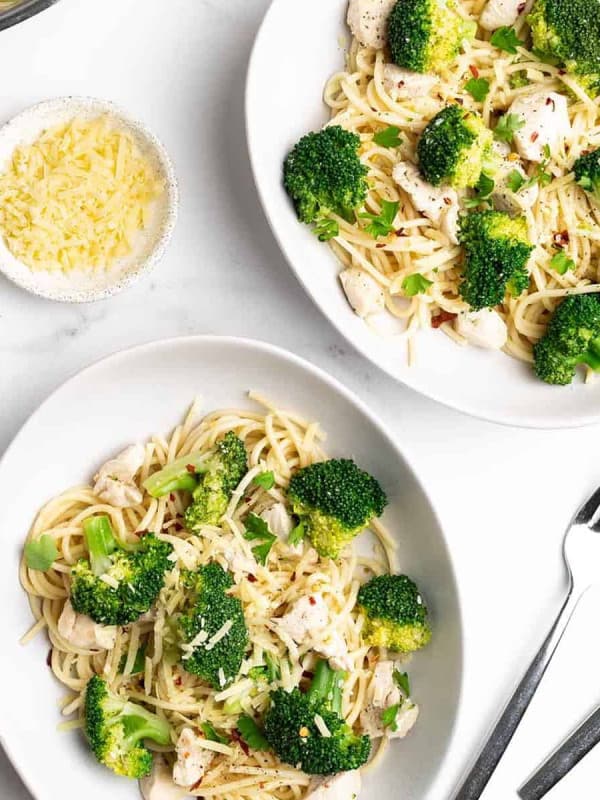 Chicken Broccoli Pasta served in oblong white bowls on a white marble surface and photographed from overhead.