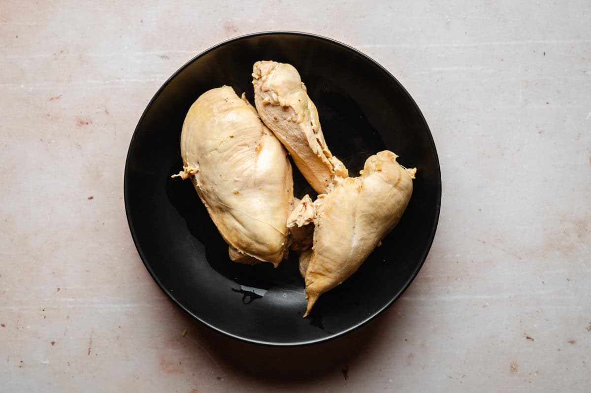 A black plate with three cooked chicken breasts on a light-colored surface.