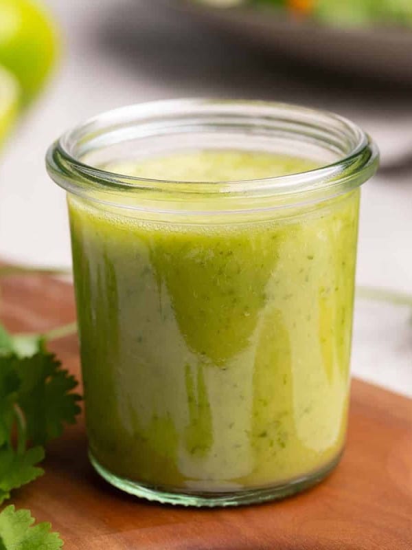 Cilantro Lime Vinaigrette in a clear glass container on a wooden board.