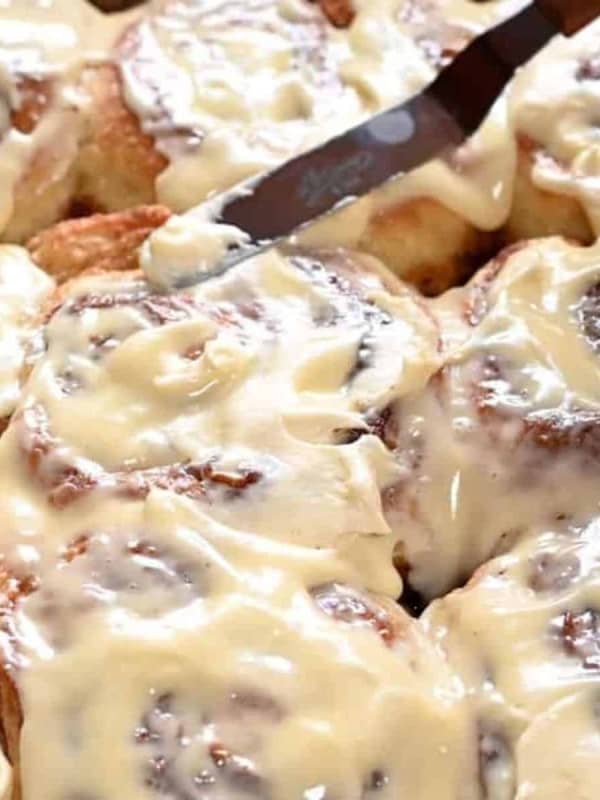 spreading cream cheese frosting on warm cinnamon rolls