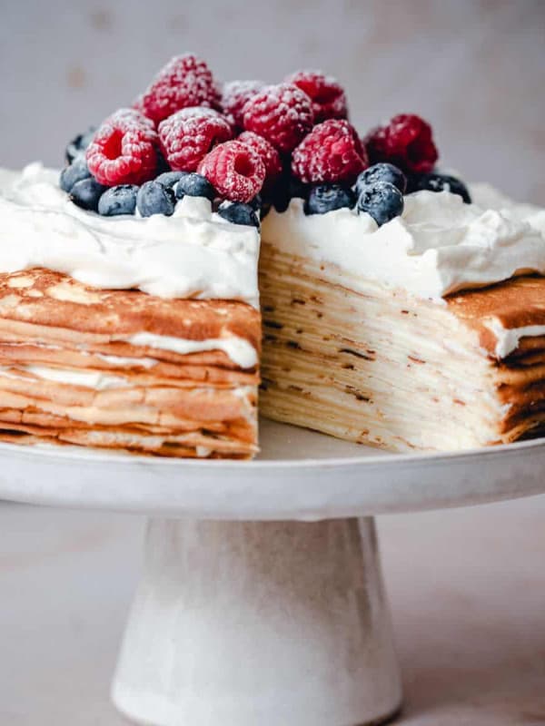 Crepe Cake served on a white ceramic cake plate with one slice cut out.