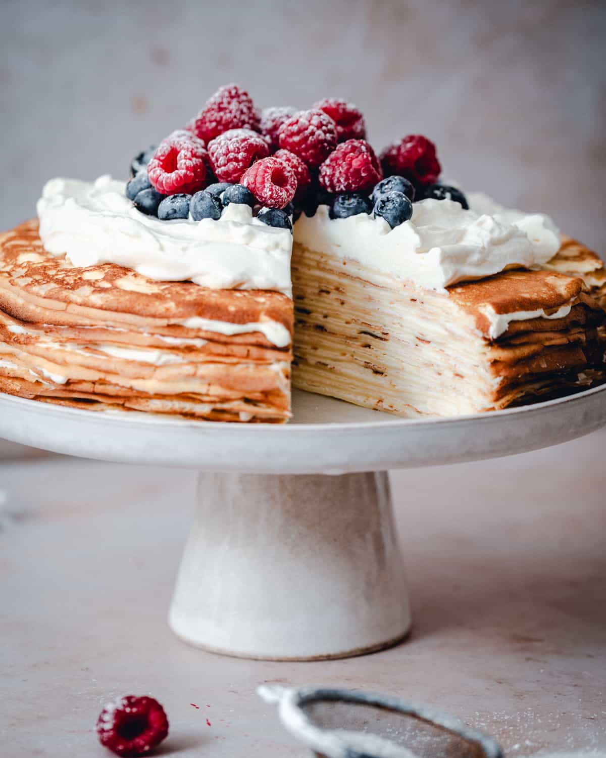 Crepe Cake served on a white ceramic cake stand with one slice cut out.