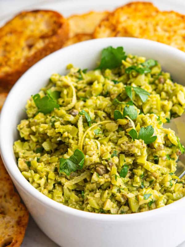 Green Olive Tapenade served in a white bowl with crostini around.