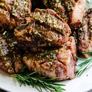 Grilled Lamb Loin Chops stacked on a white platter with rosemary sprigs.