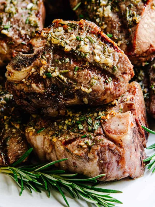 Grilled Lamb Loin Chops stacked on a white platter with rosemary sprigs.