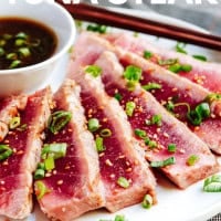 A plate of sliced grilled tuna steak, garnished with chopped green onions and accompanied by a small bowl of dipping sauce. The text "GRILLED TUNA STEAK" is displayed at the top of the image, with the website "pinchandswirl.com" noted at the bottom.