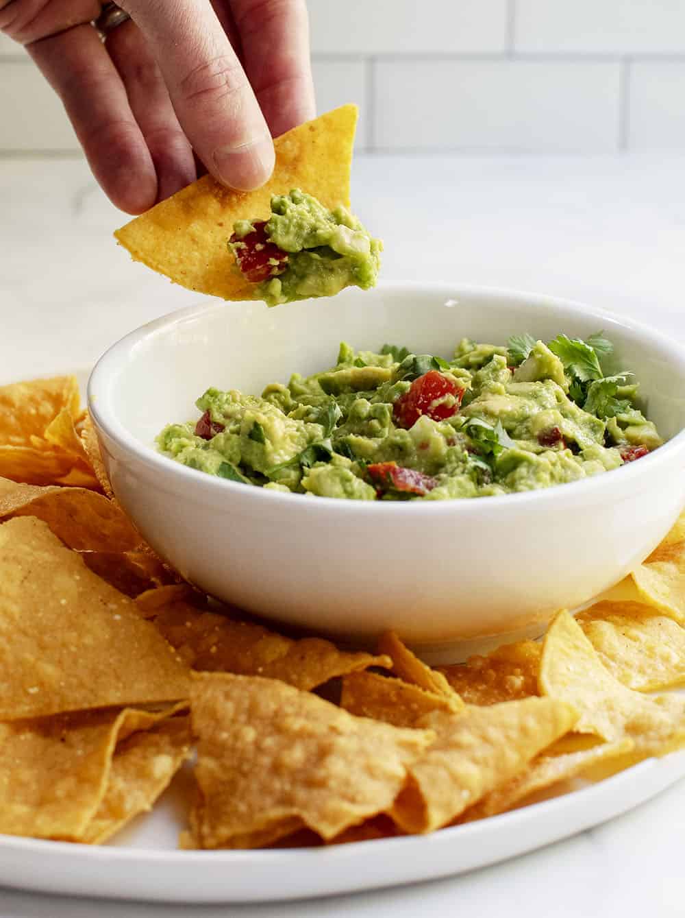 dipping chip into Salsa Guacamole in a white bowl