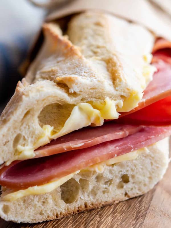 Brown paper parchment wrapped Jambon Beurre sandwich on a wooden board.