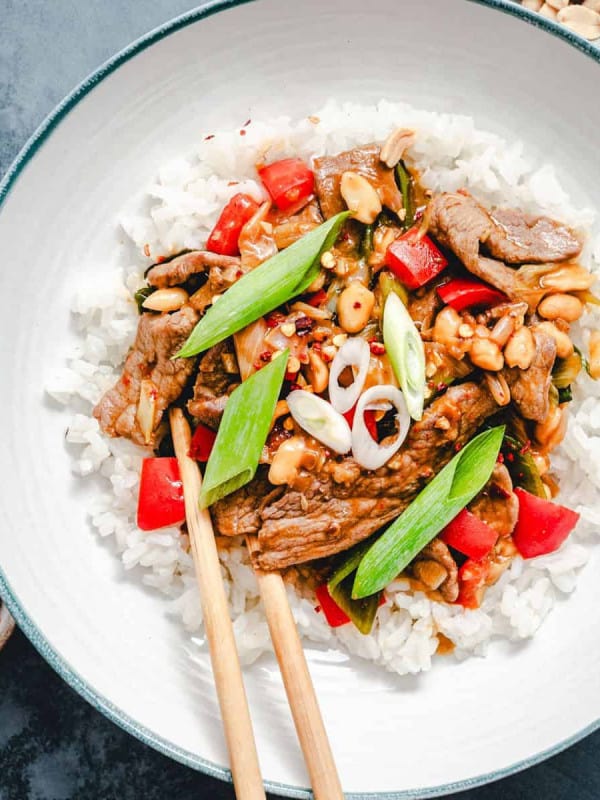 Kung Pao Beef served in a white ceramic bowl with wooden chopsticks and peanuts in a bowl and photographed from the top.