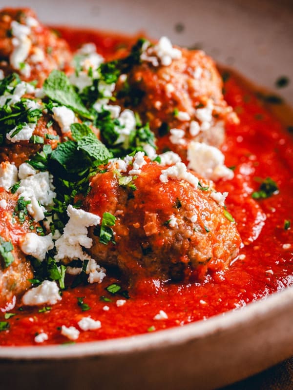 Five Lamb Meatballs served in red sauce and photographed at an angle.