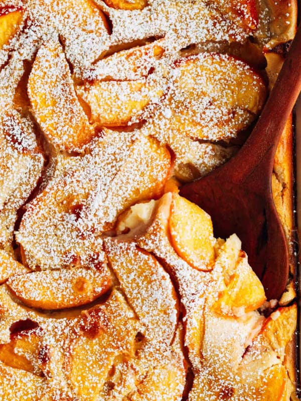 Peach Clafoutis, photographed from above, baked in a white ceramic baking dish served with a wooden serving spoon.