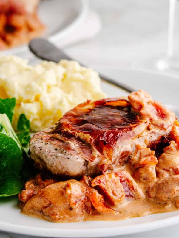 Pork Saltimbocca served on a white plate with greens and mashed potatoes.