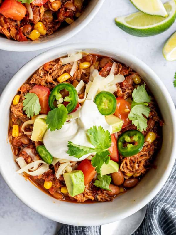 Pulled Pork Chili served in white bowls with lime wedges, photographed from above.