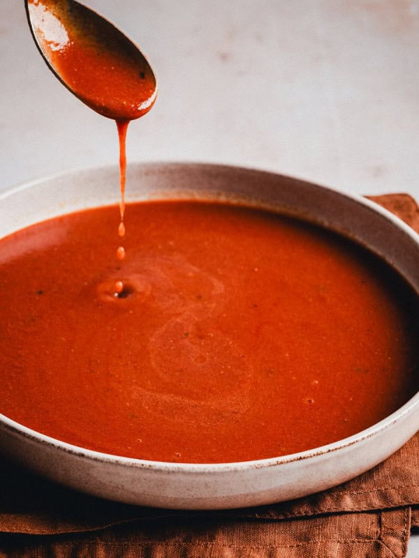 Homemade Red Enchilada Sauce dripping from a spoon over a bowl.