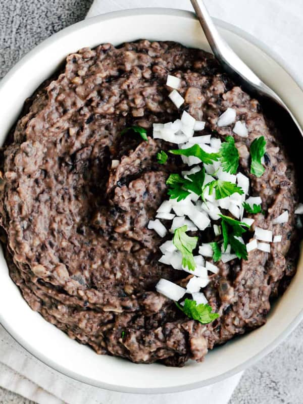 Refried Black Beans in a white bowl with a stainless steel serving spoon.