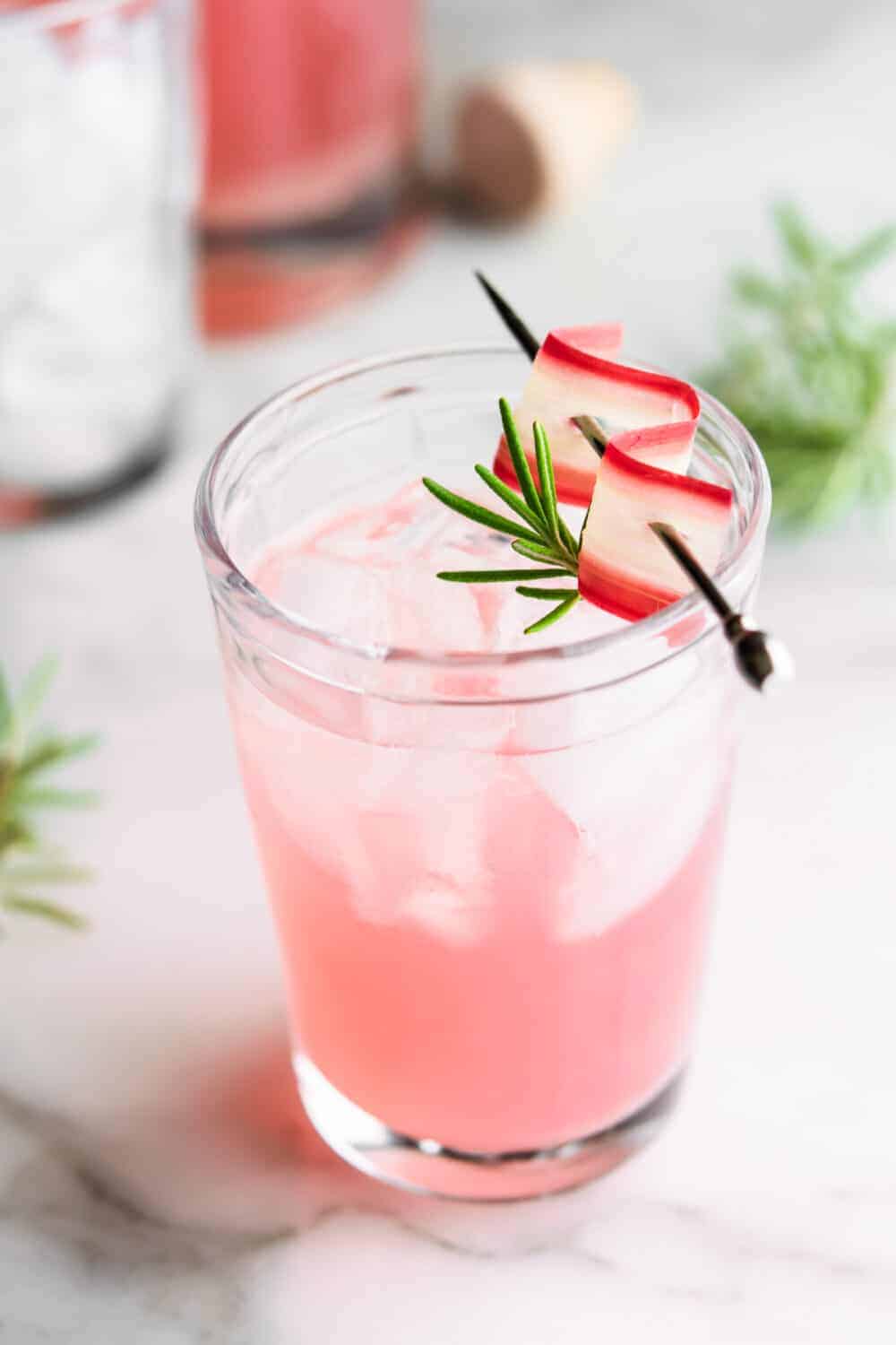 Rhubarb Cocktail over ice in a clear glass with rhubarb and rosemary garnish