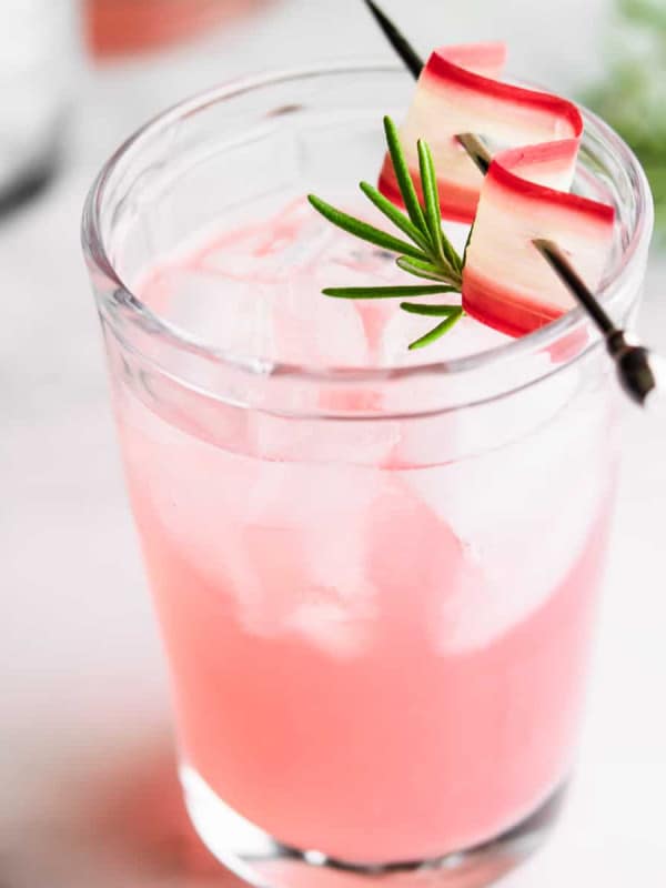 Rhubarb Cocktail over ice in a clear glass with rhubarb and rosemary garnish