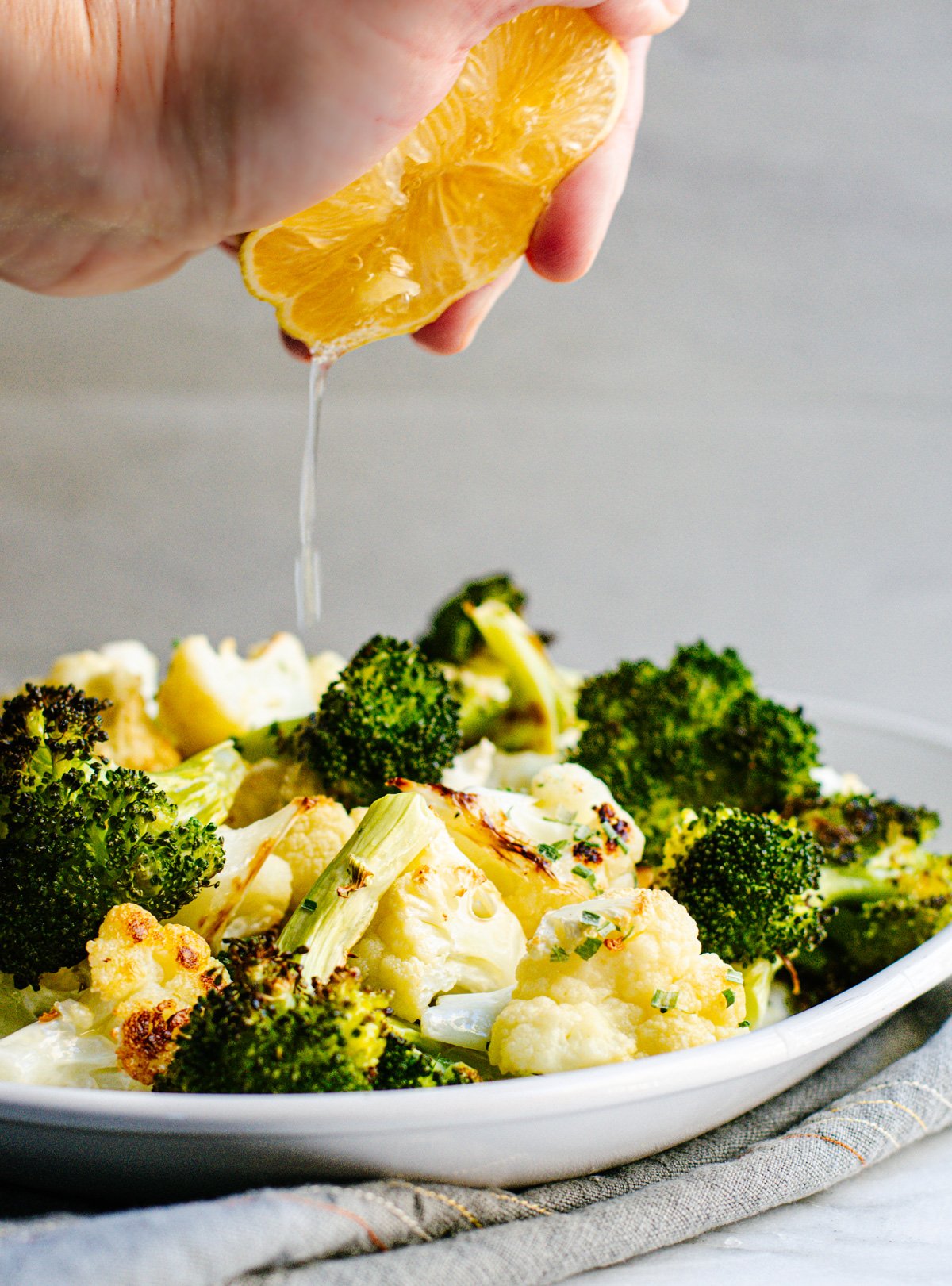 Squeezing lemon over Roasted Broccoli and Cauliflower on a white platter.