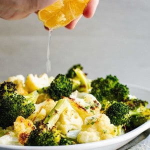 Squeezing lemon over Roasted Broccoli and Cauliflower on a white platter.