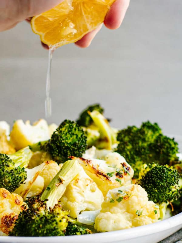 Squeezing lemon over Roasted Broccoli and Cauliflower on a white platter.