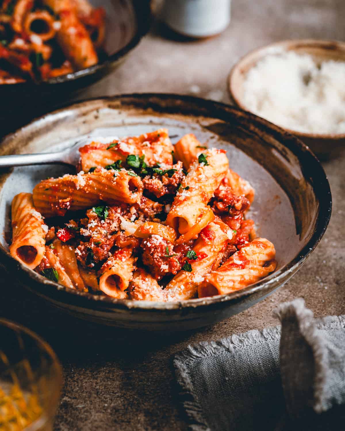 Sausage and Peppers Pasta served in a dark bowl in a moody scene and photographed from an angle.