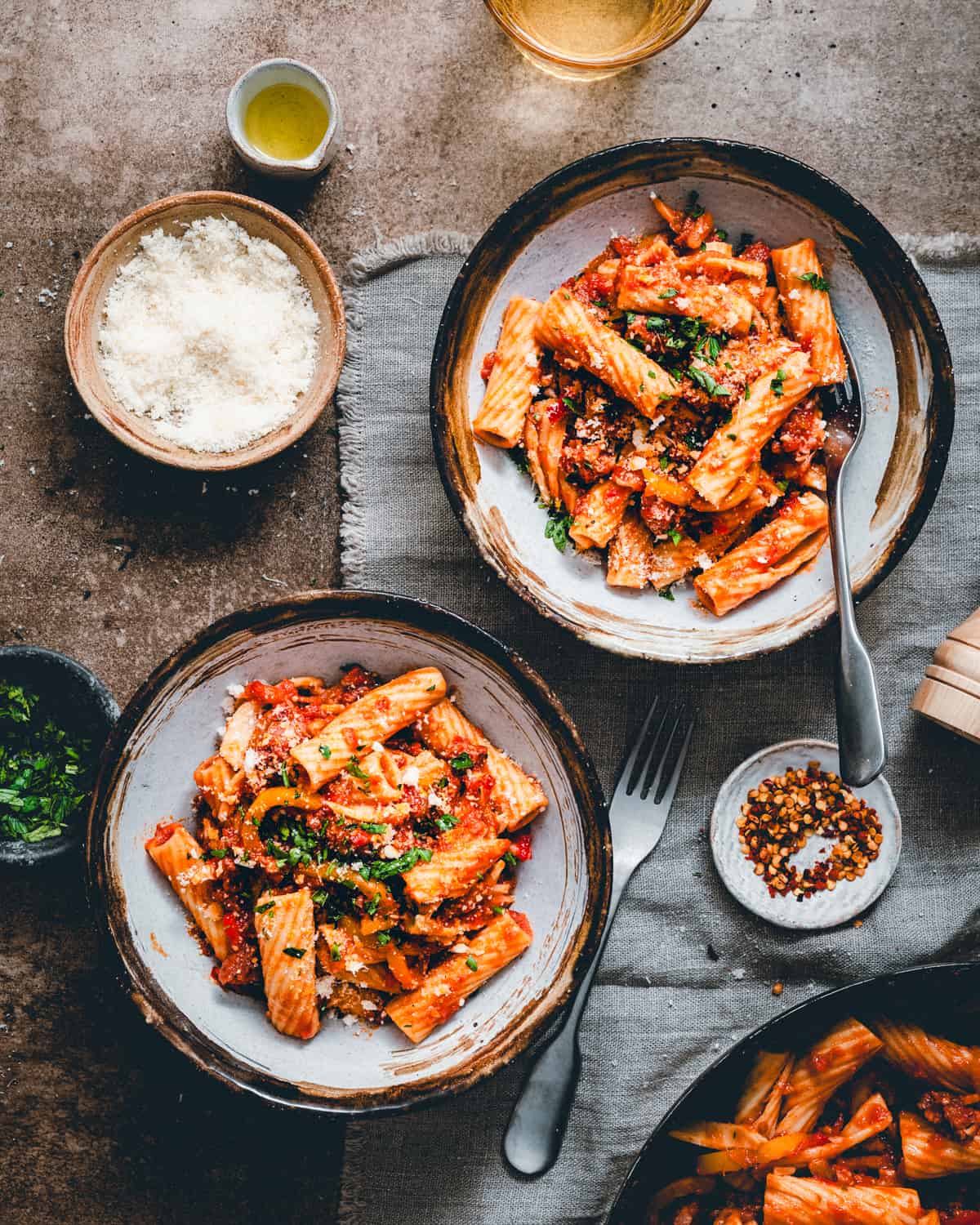 Two bowls of Sausage and Peppers Pasta served in dark bowls in a moody scene and photographed from the top.