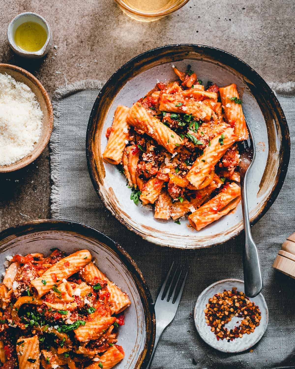 Two bowls of Sausage and Peppers Pasta served in dark bowls in a moody scene and photographed from the top.