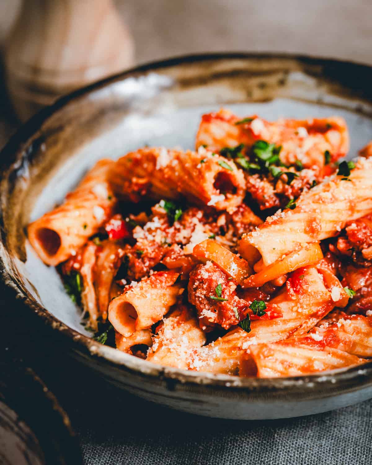 Sausage and Peppers Pasta served in a dark bowl in a moody scene and photographed from an angle.