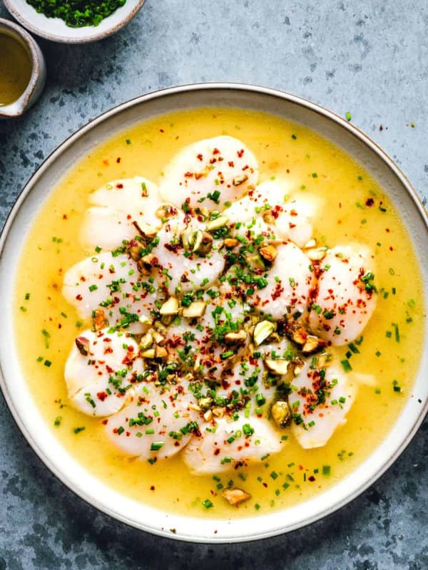 Scallop Crudo served on a white ceramic plate and photographed from overhead.